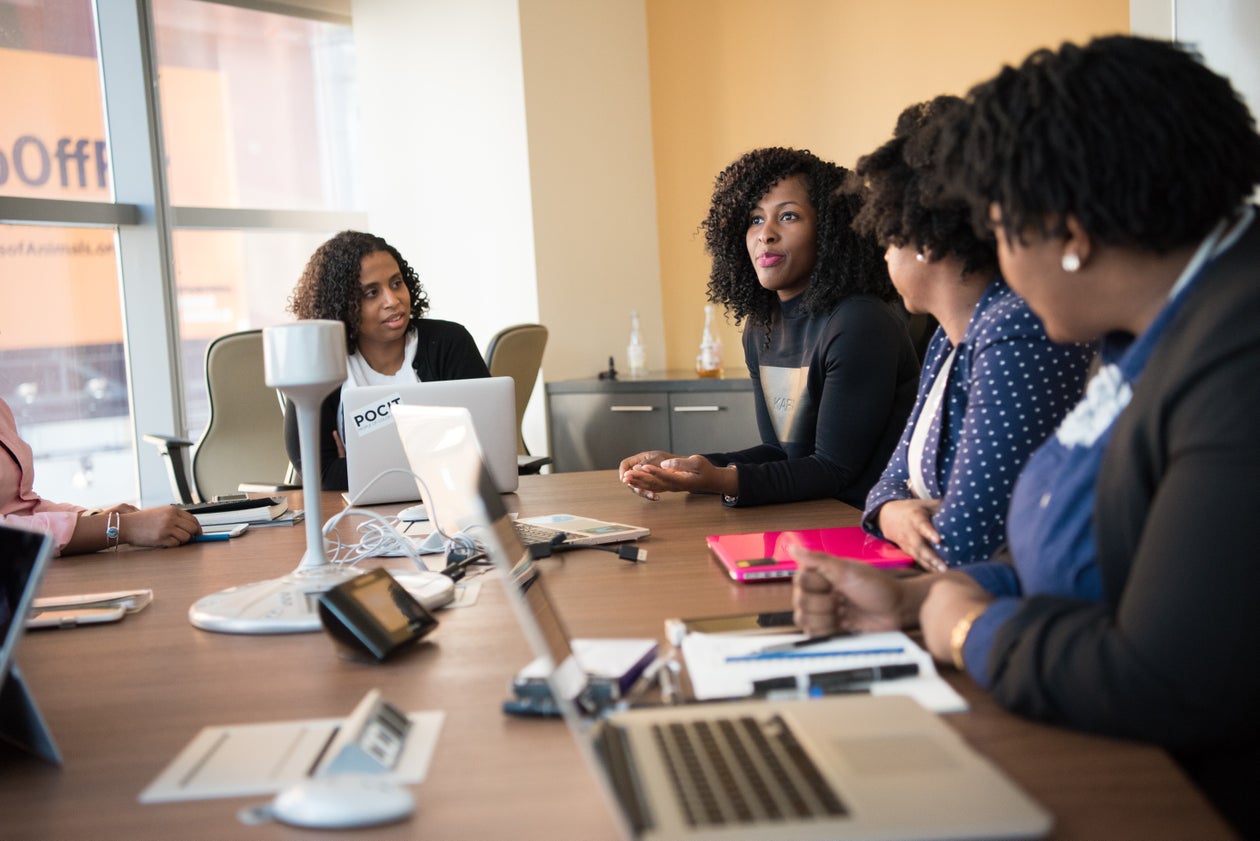 Black women talking and collaborating across a worktable